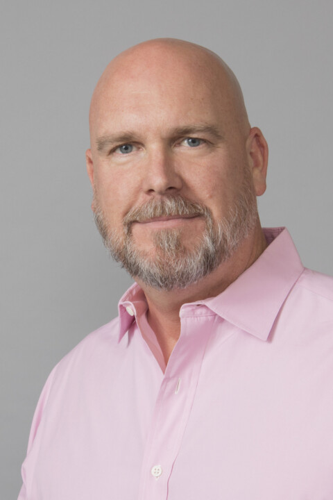 A bald man with a beard wearing a pink shirt.