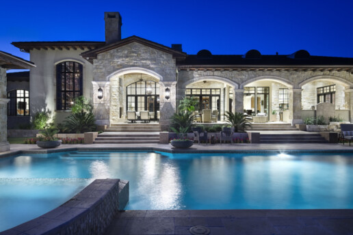 a large estate with a pool and all interior lights inside shining brightly.