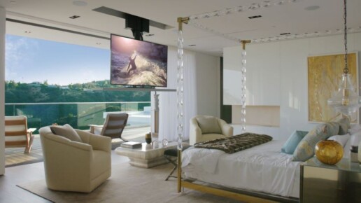 A once hidden TV hanging down from the ceiling in a luxury bedroom with floor-to-ceiling windows.