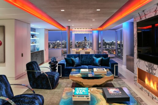 Modern living area with a flat-screen TV, view of the city, and LED-colored lights highlighting columns and the ceiling.