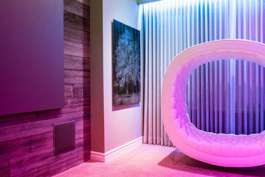 A close-up of part of a room lit by pink, purple, and blue LED lights with a flat-screen TV and an in-wall speaker.
